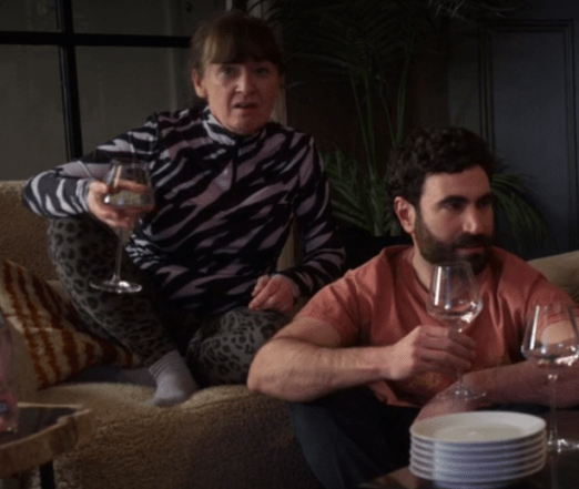 a woman and man sitting on a couch holding wine glasses