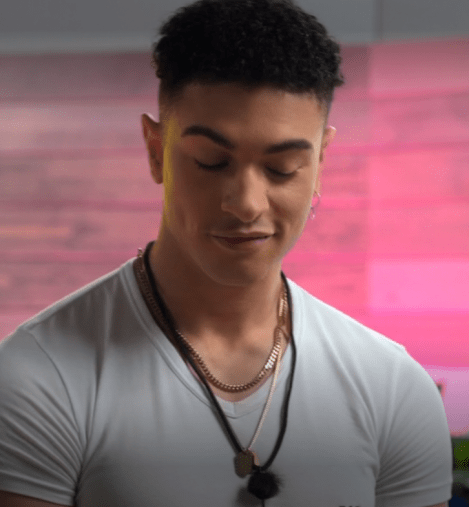 man in white shirt with several necklaces and an earring looking down