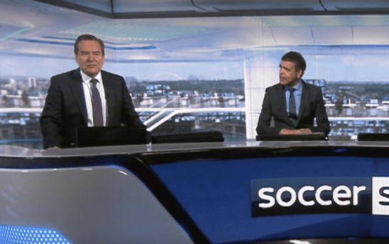 two men in suits behind a sports desk